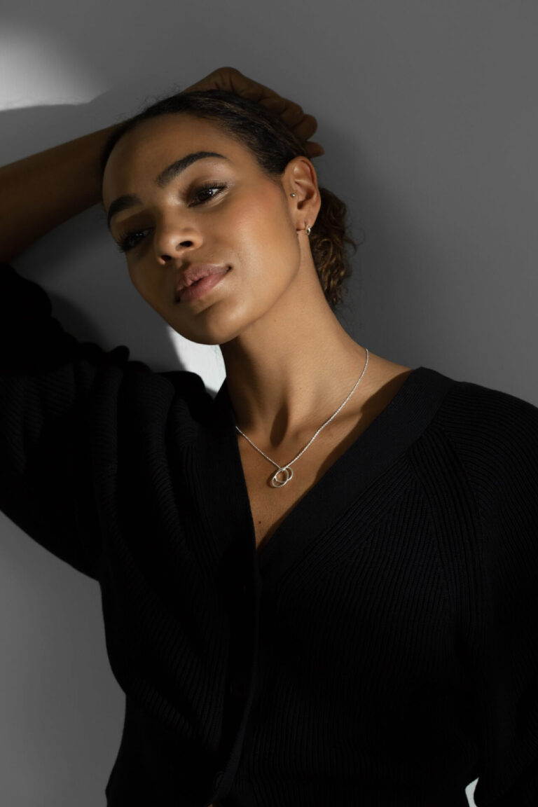 Model with darker skin wears Silver Double Charm Verona Necklace and Silver Tula Earrings, and v-neck black top