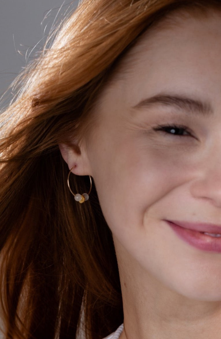 Close up of our smiling model with red hair wears Moonstone Gold Hoop Earrings and a white tank top