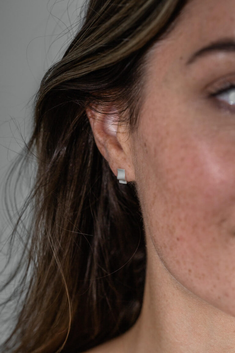 Close up of model with freckles and brown hair wearing Silver Wave Studs