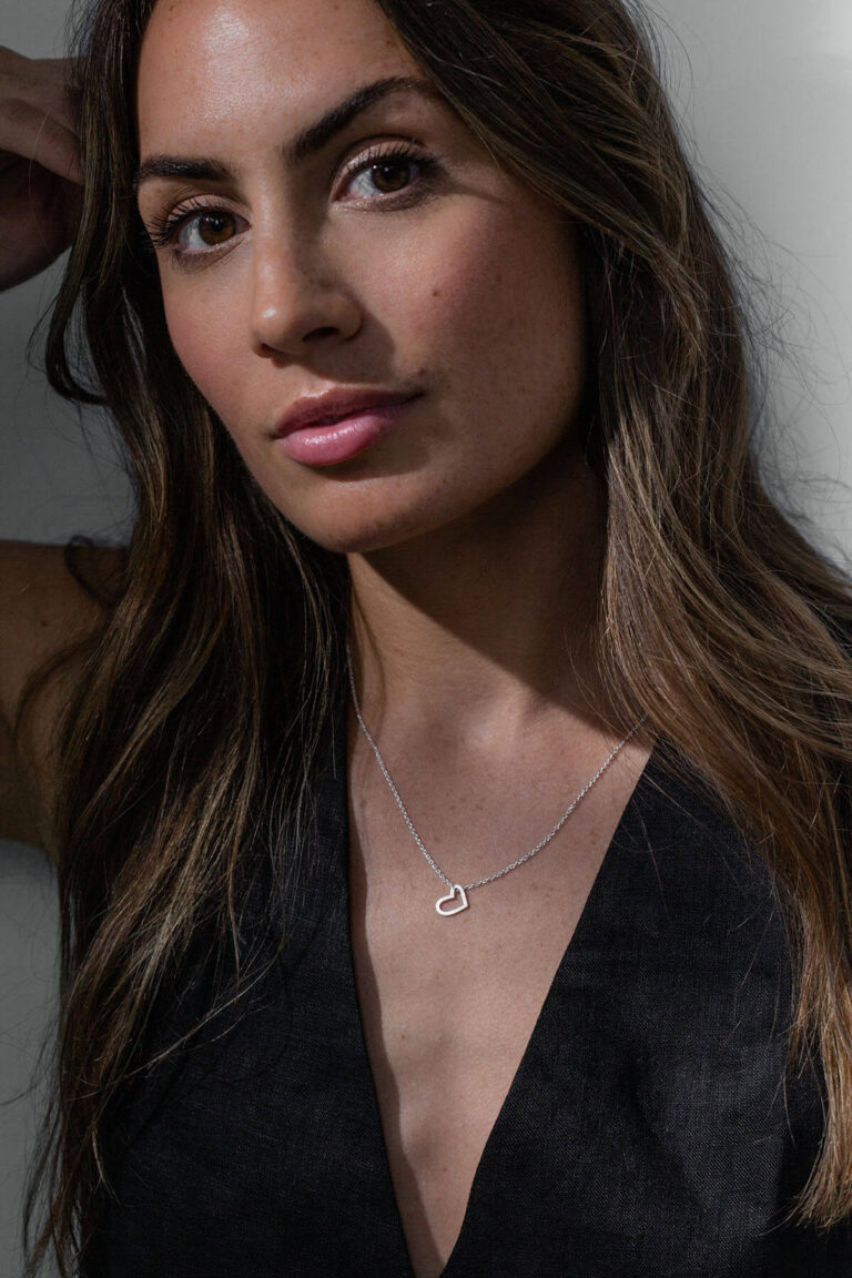 Model wears silver heart Cupid necklace and black deep v-neck top