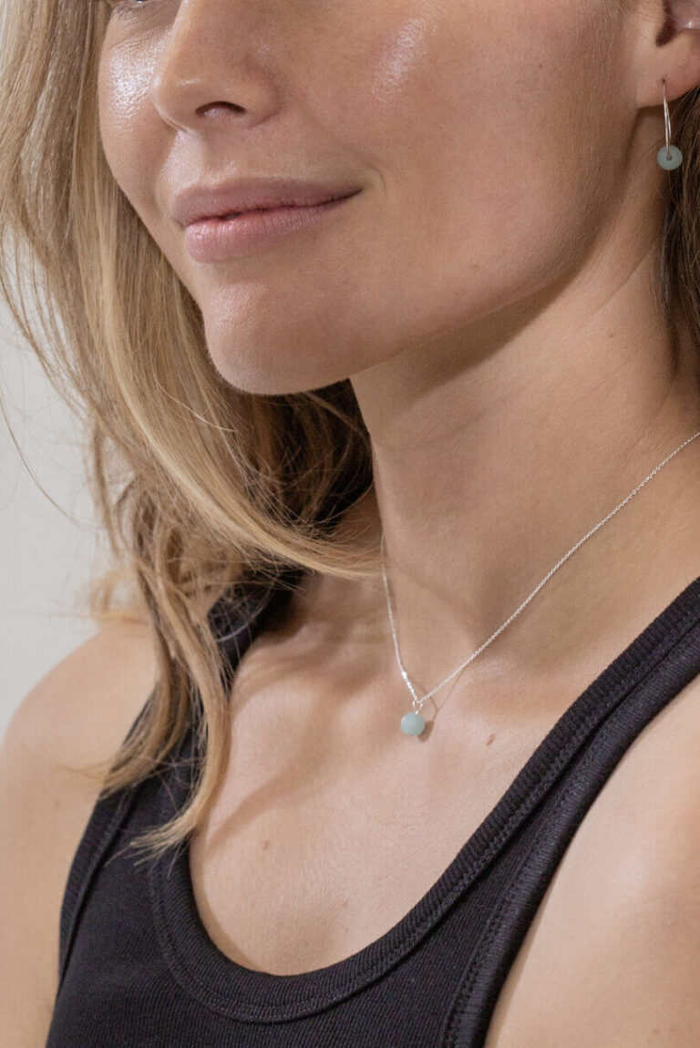 Model with blonde hair wearing Pacific Blue Seaglass Necklace and Pacific Blue Seaglass Earrings and a black tank top