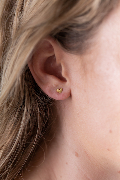 Close up of Gold Tiny Heart Stud Earrings worn by model with blonde hair
