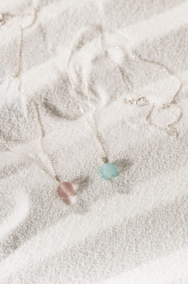 Periwinkle Pink Seaglass Necklace and Pacific Blue Seaglass Necklace on sand